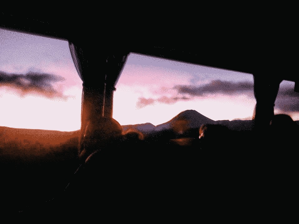 A dormant volcano through a bus window, with the sun setting behind it.